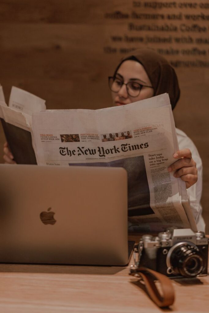 Muslim woman reading The New York Times behind a laptop in a cozy setting.